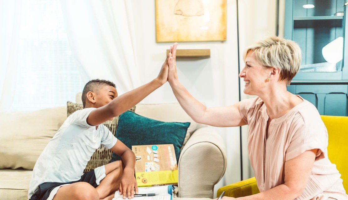 Smiling mom high-fiving her son over homework in a bright living room