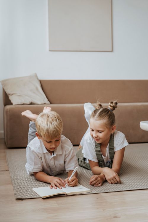 Siblings doing homework together on the living room floor